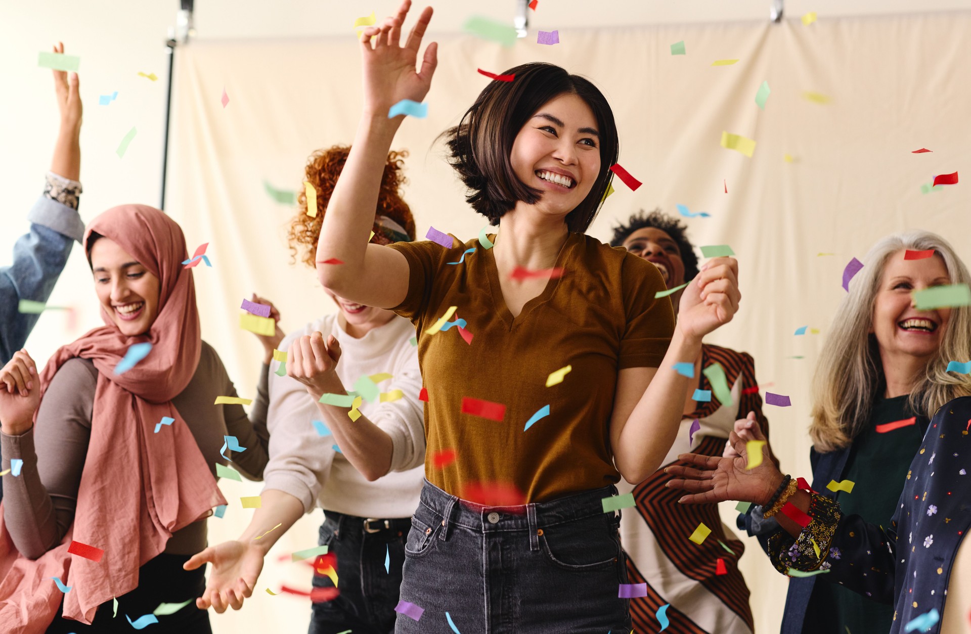 Action shot of mixed age multiethnic women celebrating International Women's Day by dancing with ticker tape